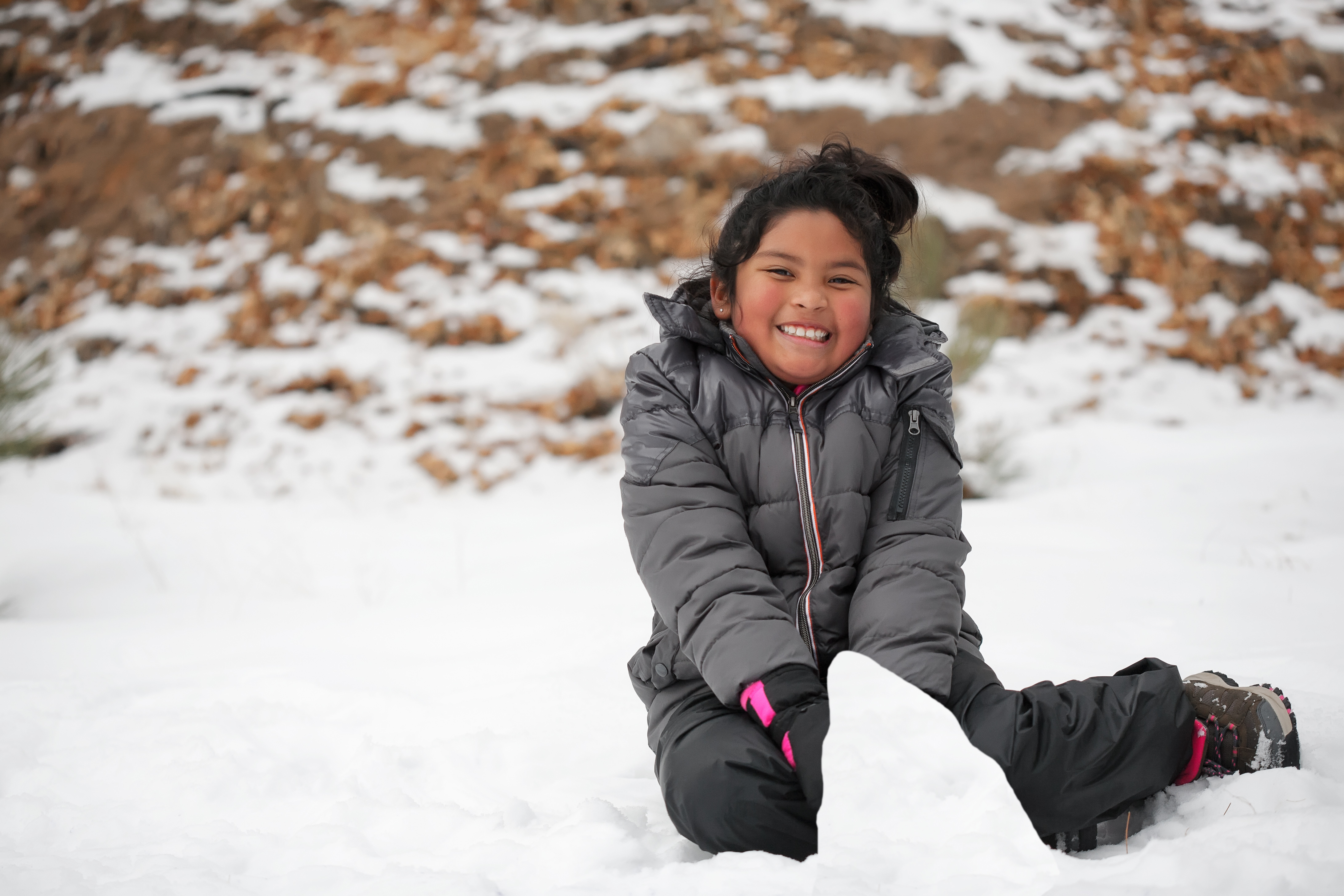 elementary girl sits in snow building snow mound